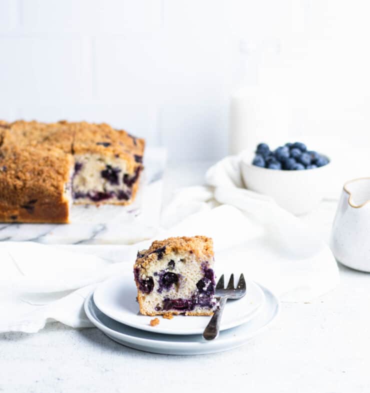 Blueberry buckle slice on two plates stacked together with the rest of the cake in the background.