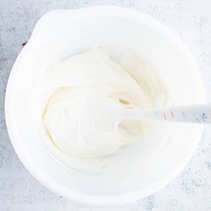 Overhead view of cream cheese glaze in a white bowl with a white spatula sticking out of it.