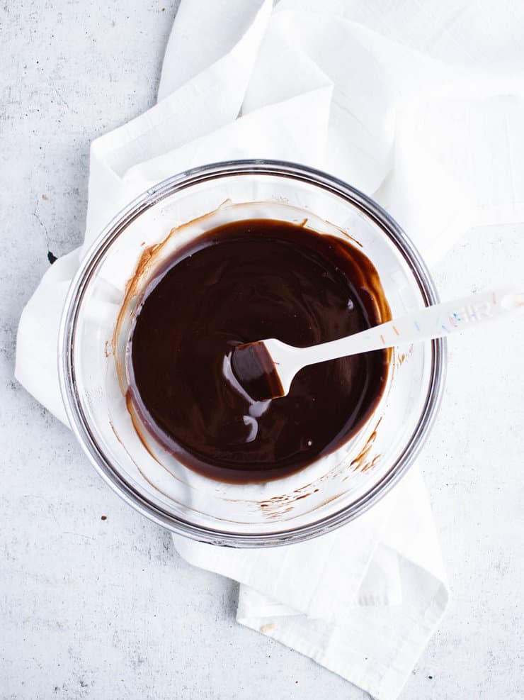 Dark chocolate ganache in a clear bowl with a white spatula sticking out to the right.
