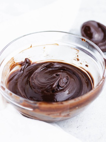 A bowl of dark chocolate ganache with a swirl on the top next to a spoon with ganache.