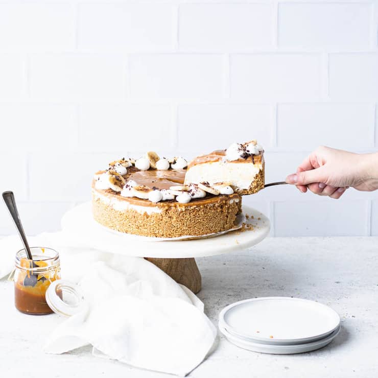 Side view of banoffee cheesecake on a marble cake stand with a slice being lifted out from the right hand side of the screen.