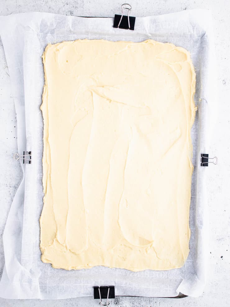 Overhead view of cake batter spread out over a parchment paper-lined baking sheet.