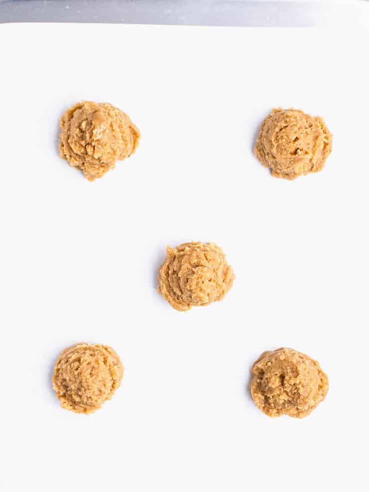 Five balls of graham cracker cookie dough on a parchment paper lined baking sheet.