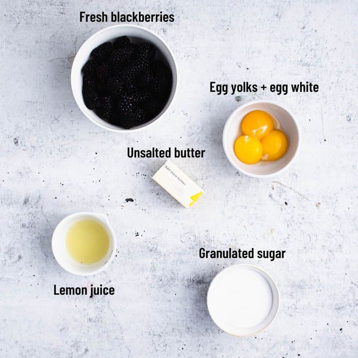 Overhead view of labeled ingredients including blackberries, lemon juice, granulated sugar, butter, egg yolks and egg white.