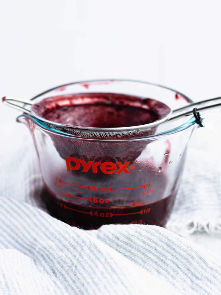 Small mesh sieve over a glass pyres measuring cup with pureed blackberry being worked through it.
