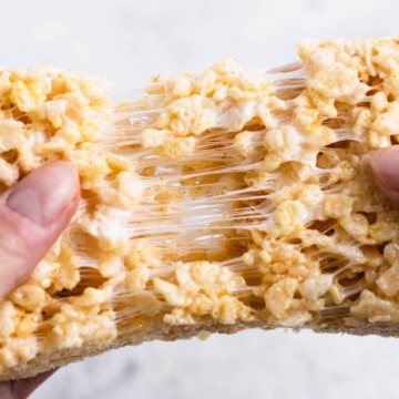 Close up of rice krispie treat being pulled in two with thick strings of marshmallow stretching between the halves.