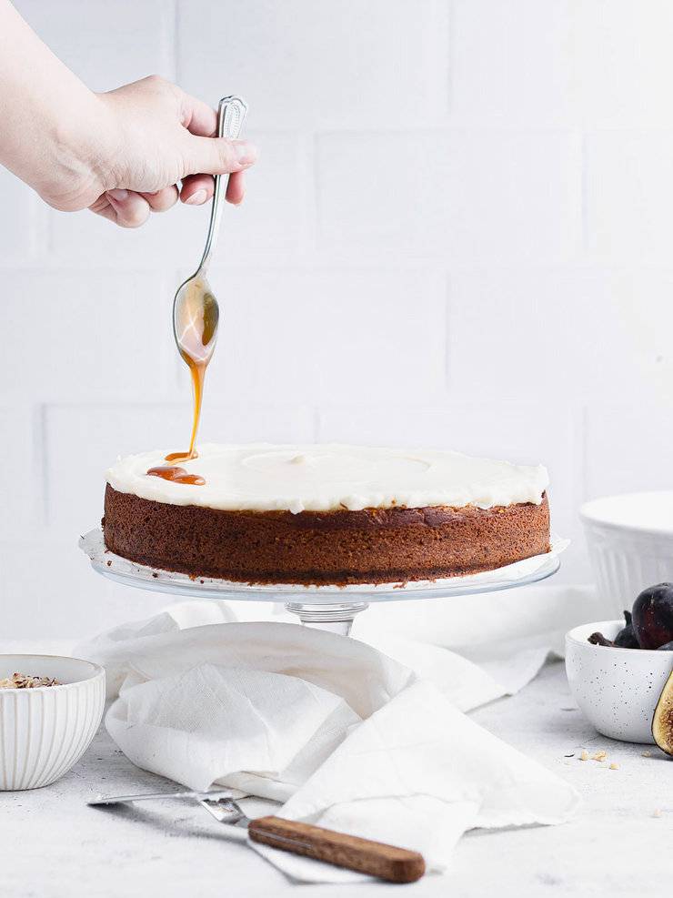 Hand drizzling caramel over a single layer spice cake topped with cream cheese frosting.