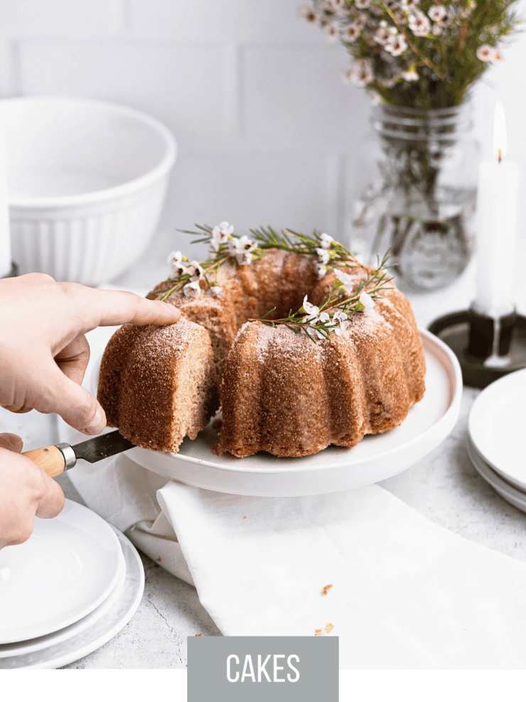 apple cider bundt cake topped with delicate flowers. A slice is being removed.